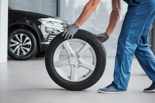 A mechanic rolling a new tire in a workshop, preparing for a tire change.