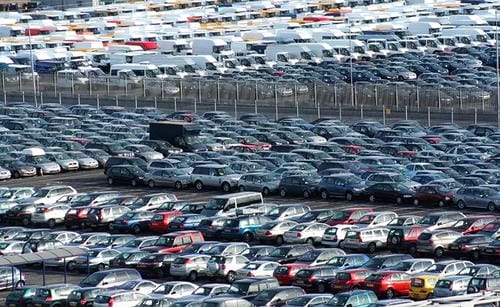 An aerial view of a massive parking lot filled with rows of cars, likely a vehicle storage facility or dealership lot.