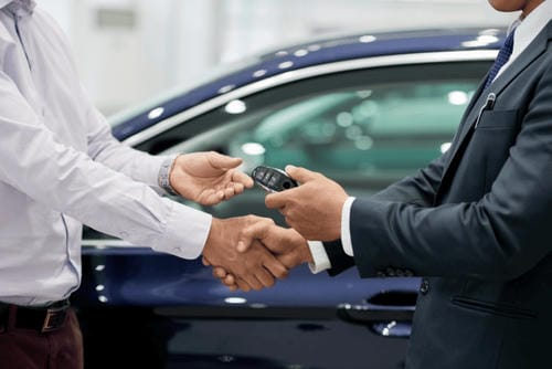 A car salesperson handing over the keys to a new owner during a handshake, signifying the car handover.