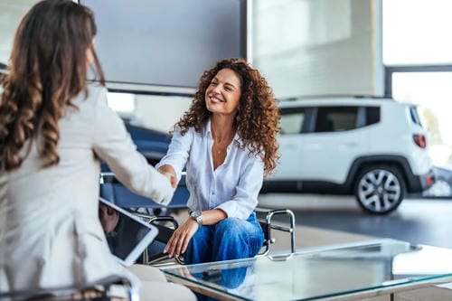 A handshake between two women at a car dealership, marking the completion of a car purchase.
