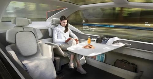 A woman reading at a fold-out table inside a concept autonomous car, showcasing a mobile office or lounge area.