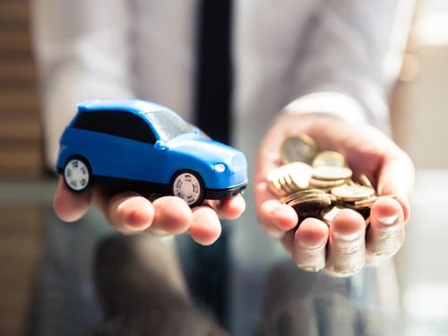 A person holding a small toy car in one hand and a handful of coins in the other, illustrating the financial trade-off of car ownership.