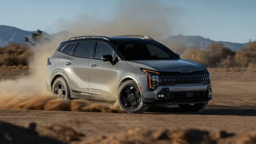 A silver Kia Sportage SUV kicking up dust while driving off-road in a desert landscape.