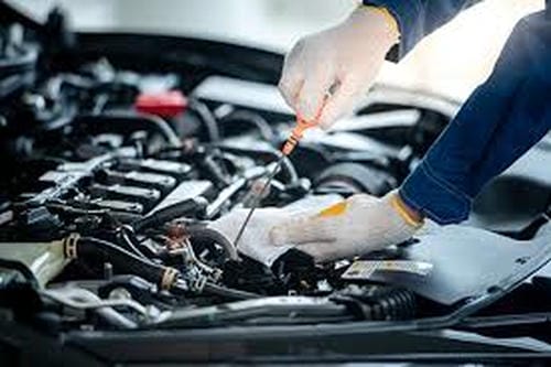 A mechanic in gloves working under the hood, using tools to perform maintenance or repairs on a car engine.