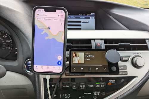 A phone displaying Google Maps navigation and a media player showing the song Softly by Clairo, mounted on a car dashboard.