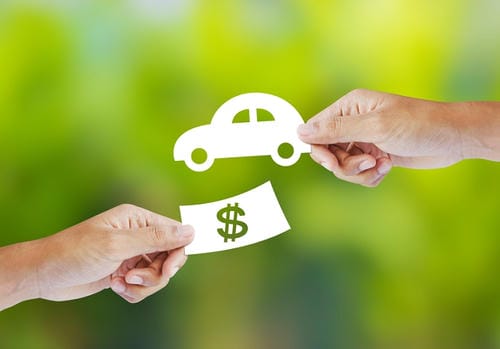 A conceptual image of hands exchanging a paper car cutout for a dollar sign, representing a car purchase or sale.