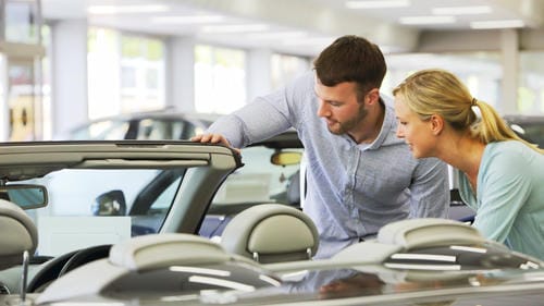 A couple examining a convertible together at a car dealership.